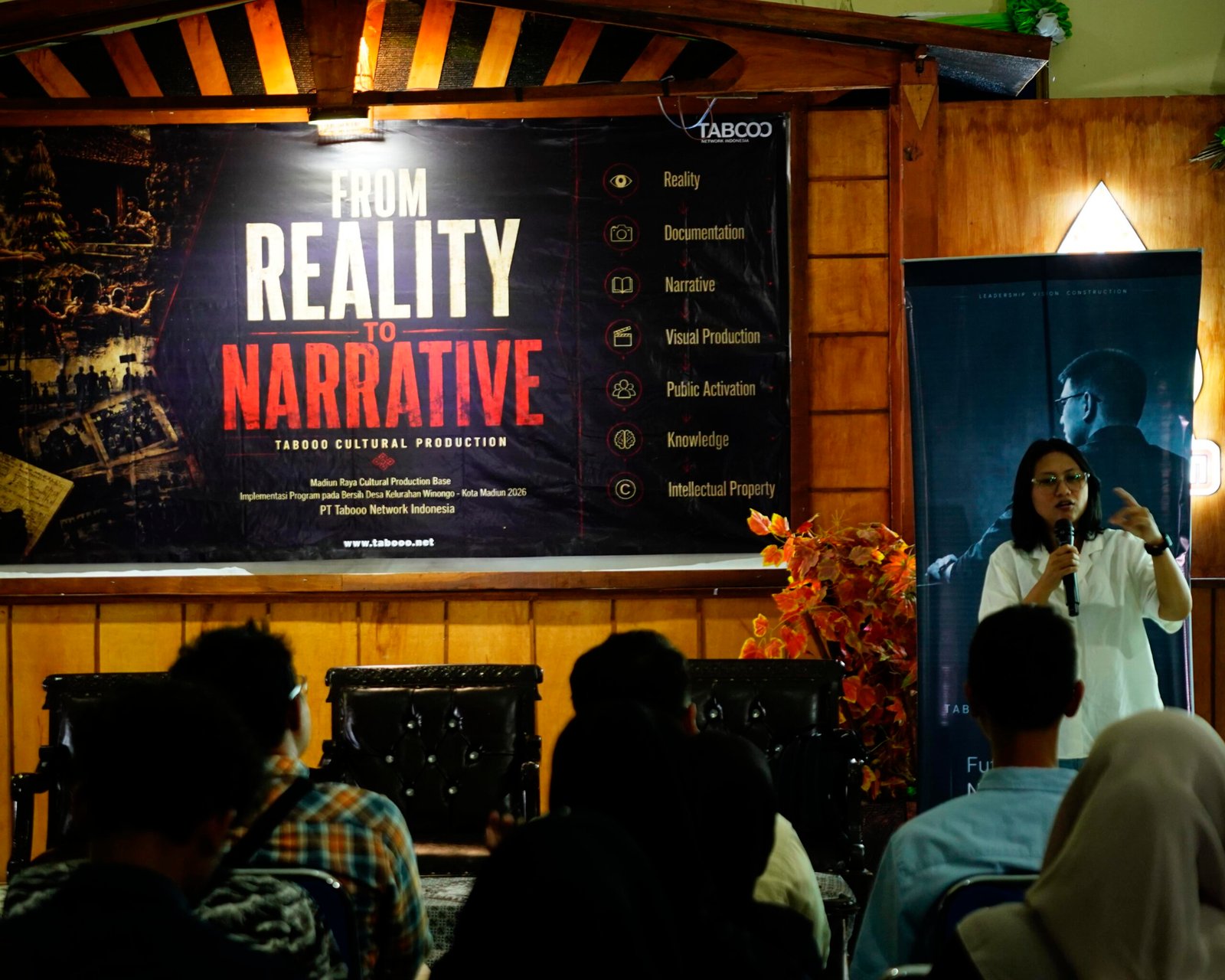 Tabooo Cinema Lab - Kota Madiun Audience seated in a hall facing a large banner that reads 'FROM REALITY TO NARRATIVE' with a speaker at a microphone on the right side of the image.