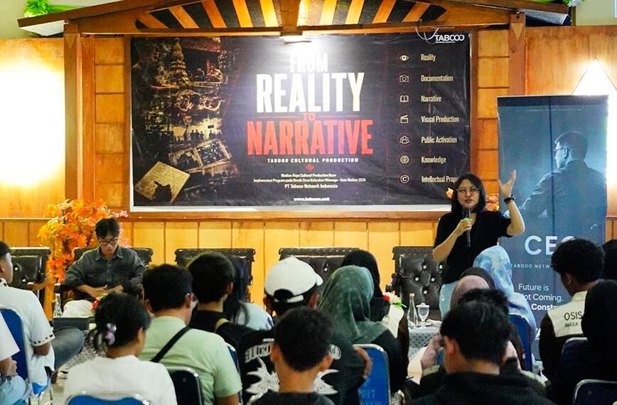 Presenter speaks into a microphone at a conference stage with a large 'From Reality to Narrative' banner behind him/her.